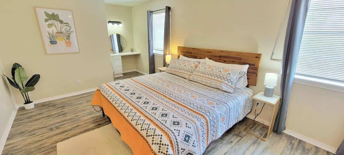 A bedroom with a bed, bedside tables, a nightstand, a mirror, and a potted plant.
