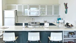 A modern kitchen with white cabinets, a central island with bar stools, a refrigerator, and a microwave. - Berghaus Pagosa - Experience the Alpenglow (Pagosa Springs)