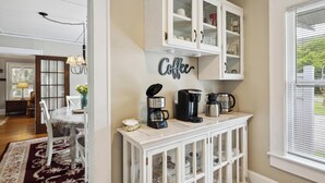 A kitchen with a coffee station, a dining table with chairs, and a cabinet with glass doors. - Historic House in Downtown Waynesville! With a firepit!  And Hot Tub 😄 (Waynesville)