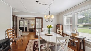 A dining area with a white table, chairs, and a chandelier. There is a fireplace, a rug, and a window with blinds. - Historic House in Downtown Waynesville! With a firepit!  And Hot Tub 😄 (Waynesville)