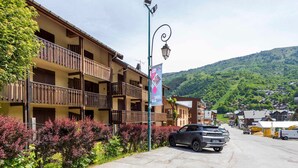 A multi-story hotel with balconies, a street in front, and a mountainous backdrop. - Studio cabin 4 ppl, parking, wifi (Valloire)