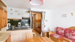 A compact kitchen with a dining table, a bunk bed, and a red patterned sofa. - Studio cabin 4 ppl, parking, wifi (Valloire)