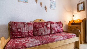 A wooden sofa bed with a red and white checkered cover, a wooden headboard, and a small wooden nightstand with a lamp. - Studio cabin 4 ppl, parking, wifi (Valloire)