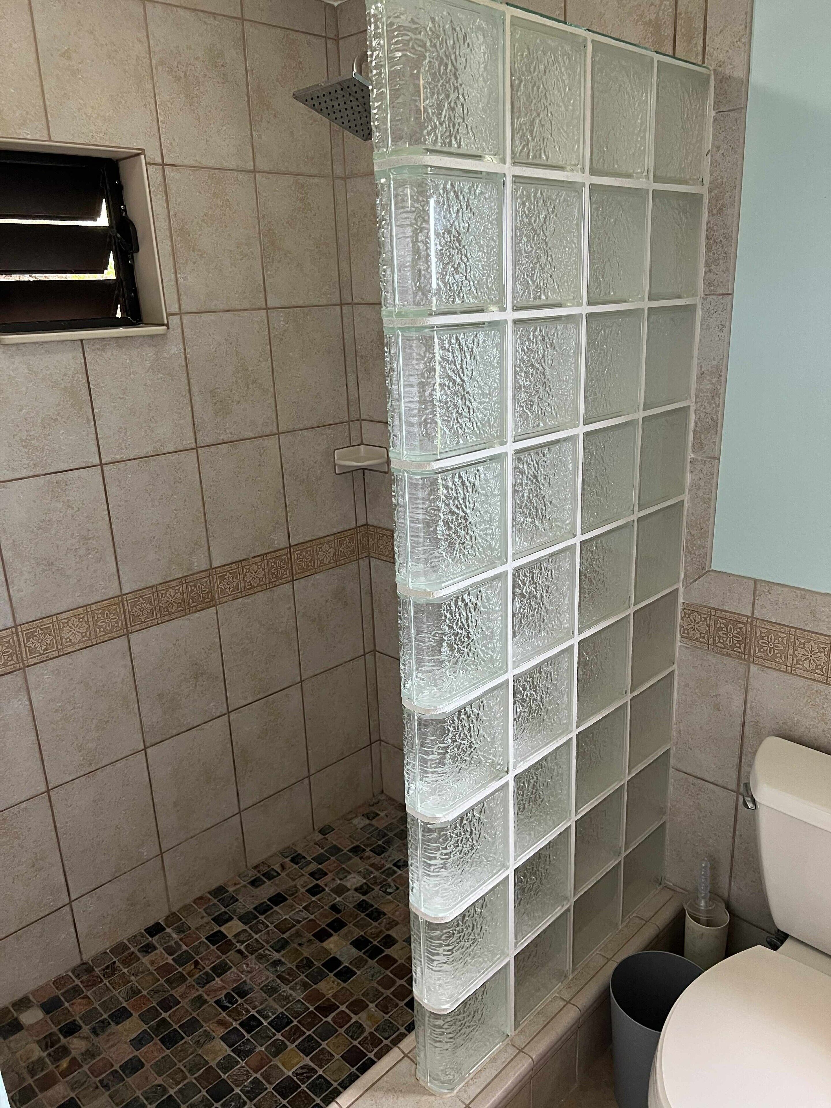 A bathroom with a glass shower enclosure, tiled walls, and a toilet.