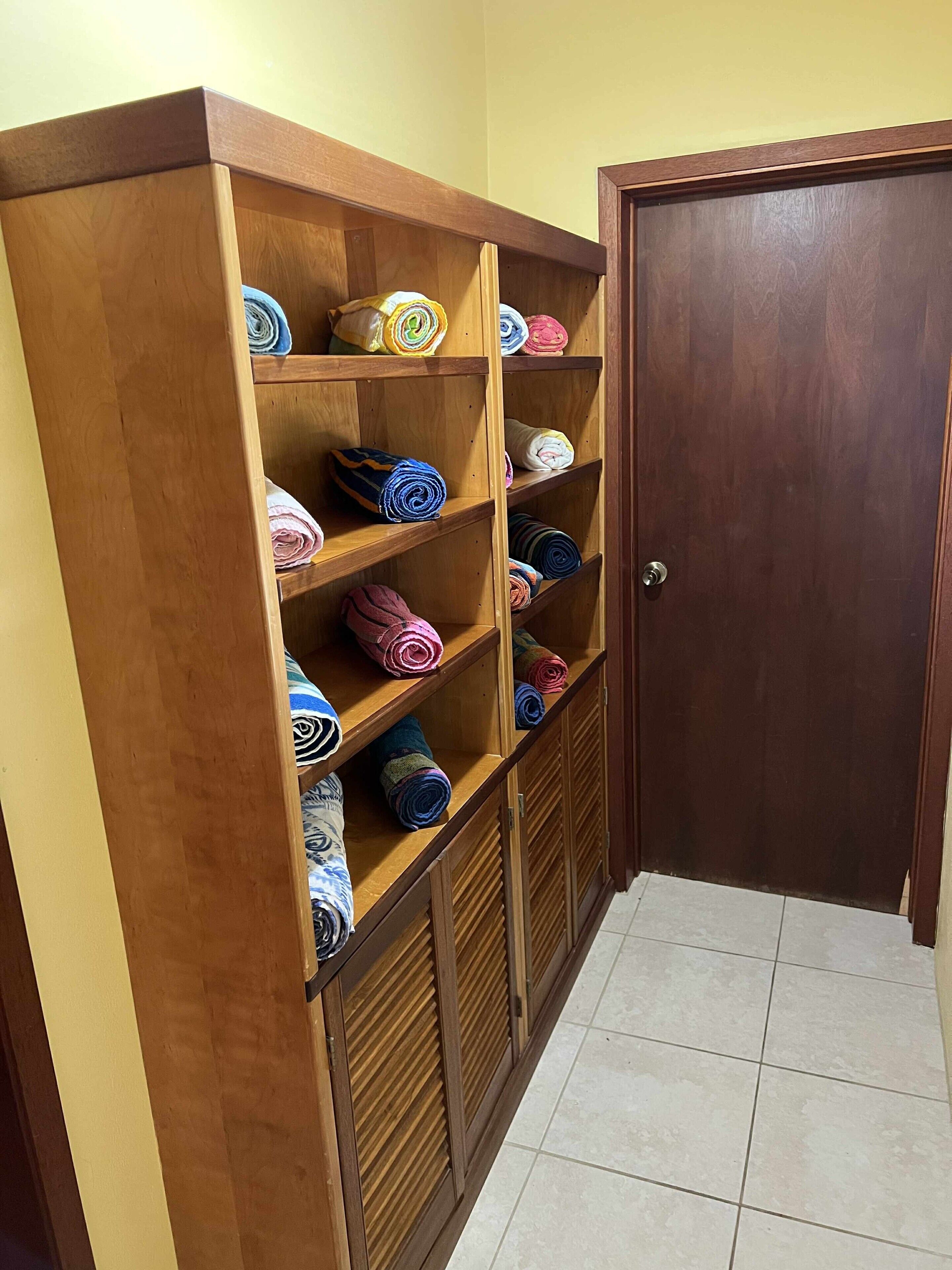 A wooden storage unit with multiple shelves holding rolled-up towels in various colors.