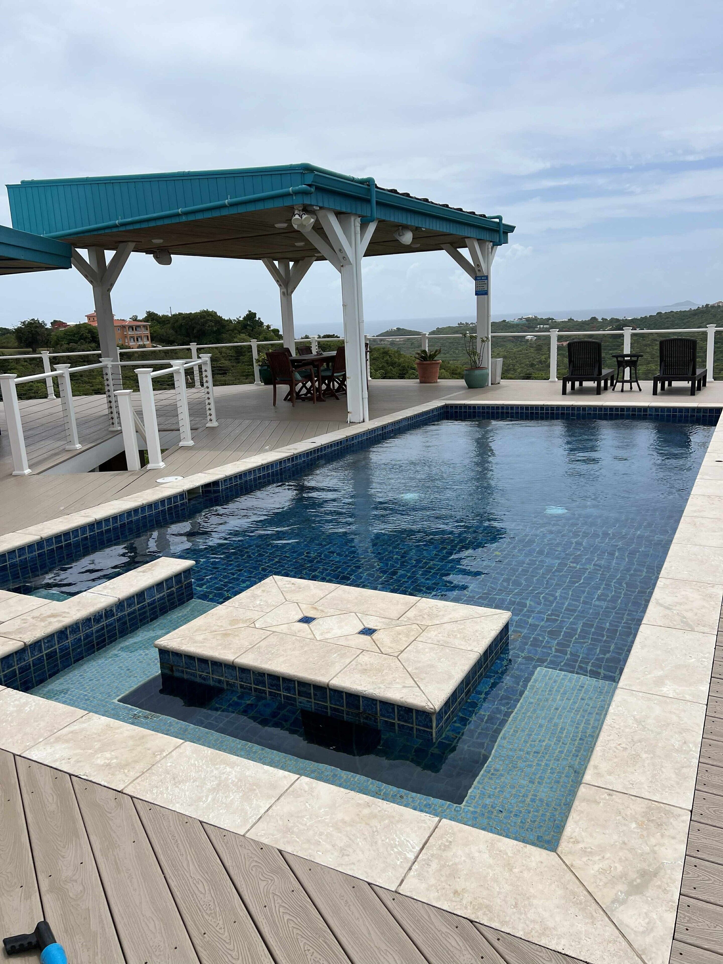 A swimming pool with a wooden deck, a covered seating area, and a view of the landscape.
