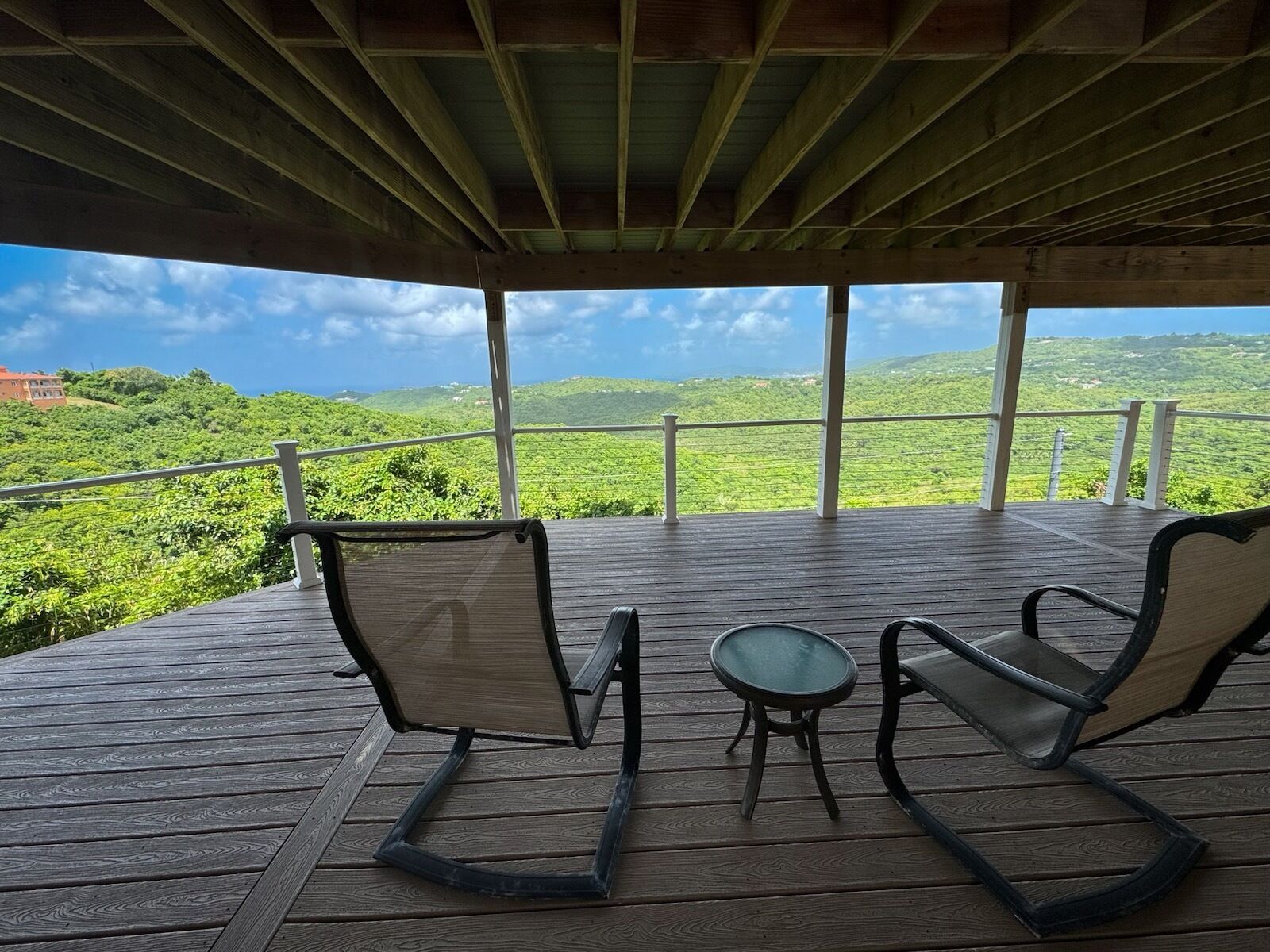 Una terraza de madera con dos sillas y una mesita, con vistas a un paisaje verde exuberante.