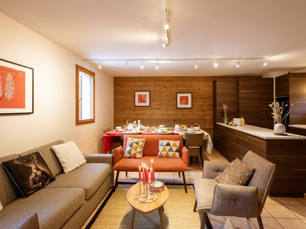 A modern living room with a sofa, armchair, and a dining area with a table set for a meal. - Chalet 5 rooms, 12 guests, pets allowed, parking (Valloire)