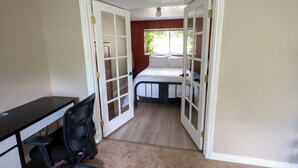 Une chambre à coucher avec un lit, un bureau et une porte ouverte donnant sur une autre pièce.