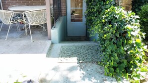 Une terrasse avec une table et des chaises en métal blanc, une porte et un mur en briques.