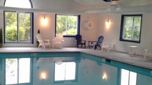 An indoor swimming pool with clear blue water, surrounded by white walls and large windows offering views of greenery. - Ski In/Ski Out Winterplace 2BR+Loft W/Fireplace, Hot Tub and Pool Access (Ludlow)