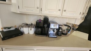 Een keuken met witte kastjes, een koffiezetapparaat, een waterkoker en potten op het aanrecht.