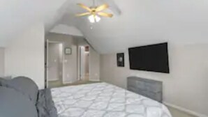 Een slaapkamer met een bed, een plafondventilator, een televisie aan de muur en een deur naar een andere kamer.