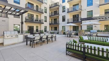 Un'area patio esterna moderna con barbecue, posti a sedere e ombrelloni.