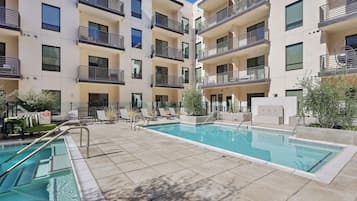 A modern apartment building with a swimming pool, outdoor seating, and balconies.