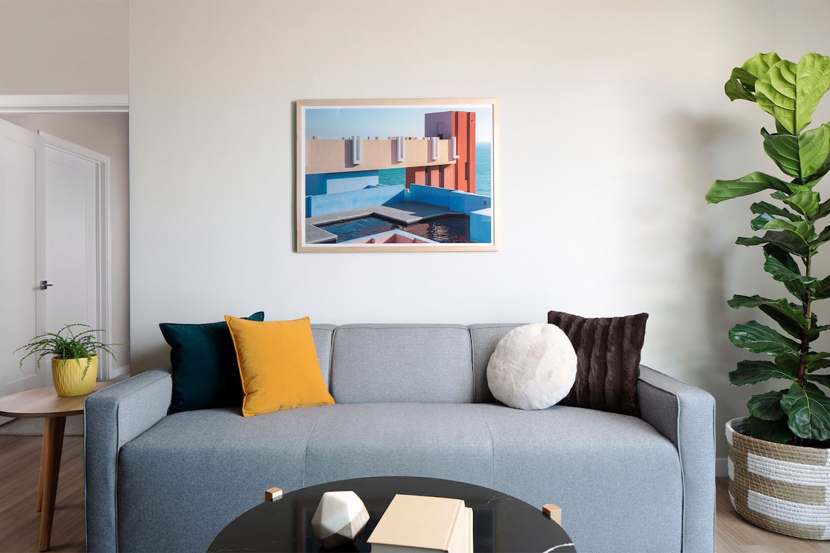 A modern living room with a grey sofa, a coffee table, and a framed abstract painting on the wall.