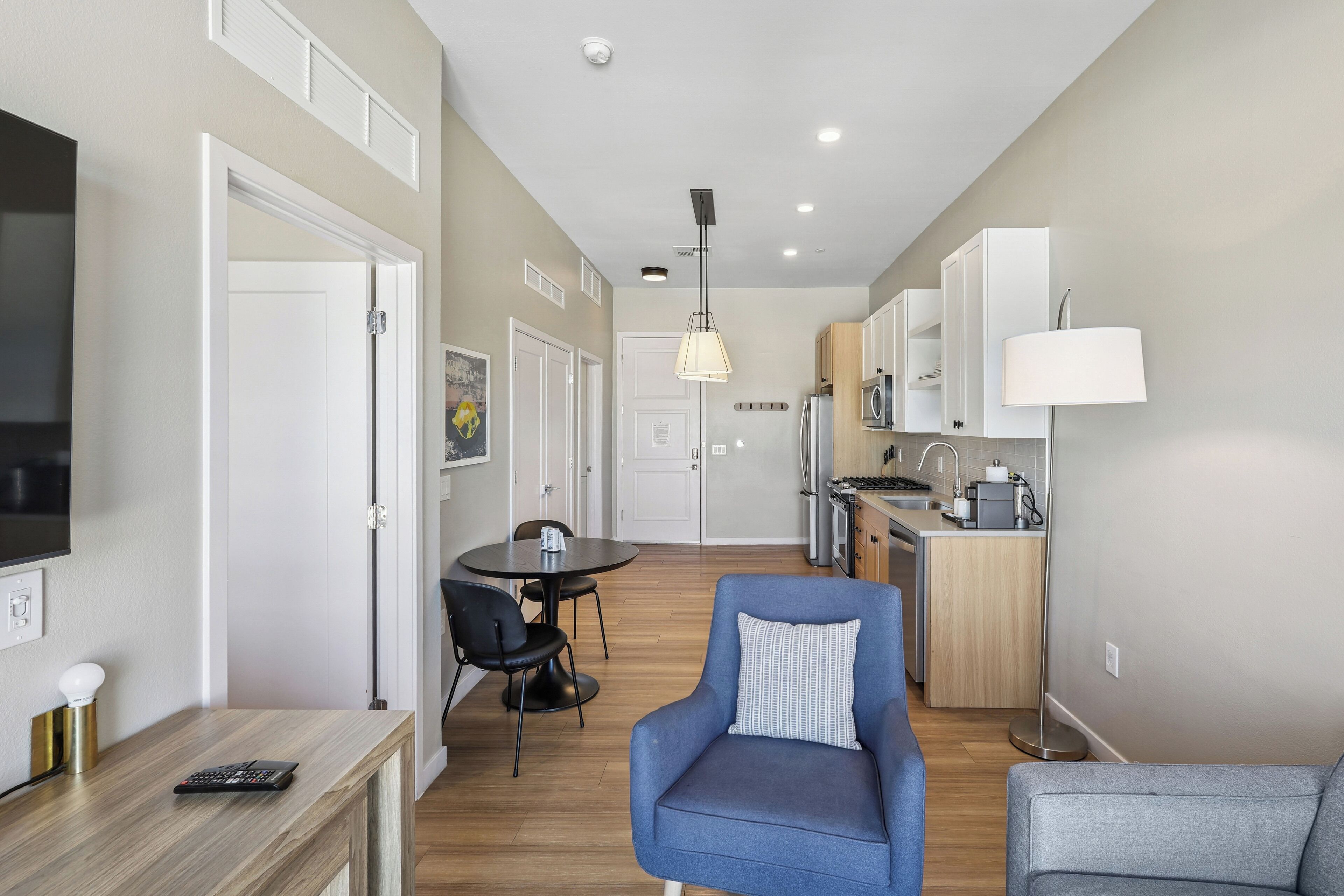 A modern apartment with a dining area, kitchenette, and a living room with a blue armchair.