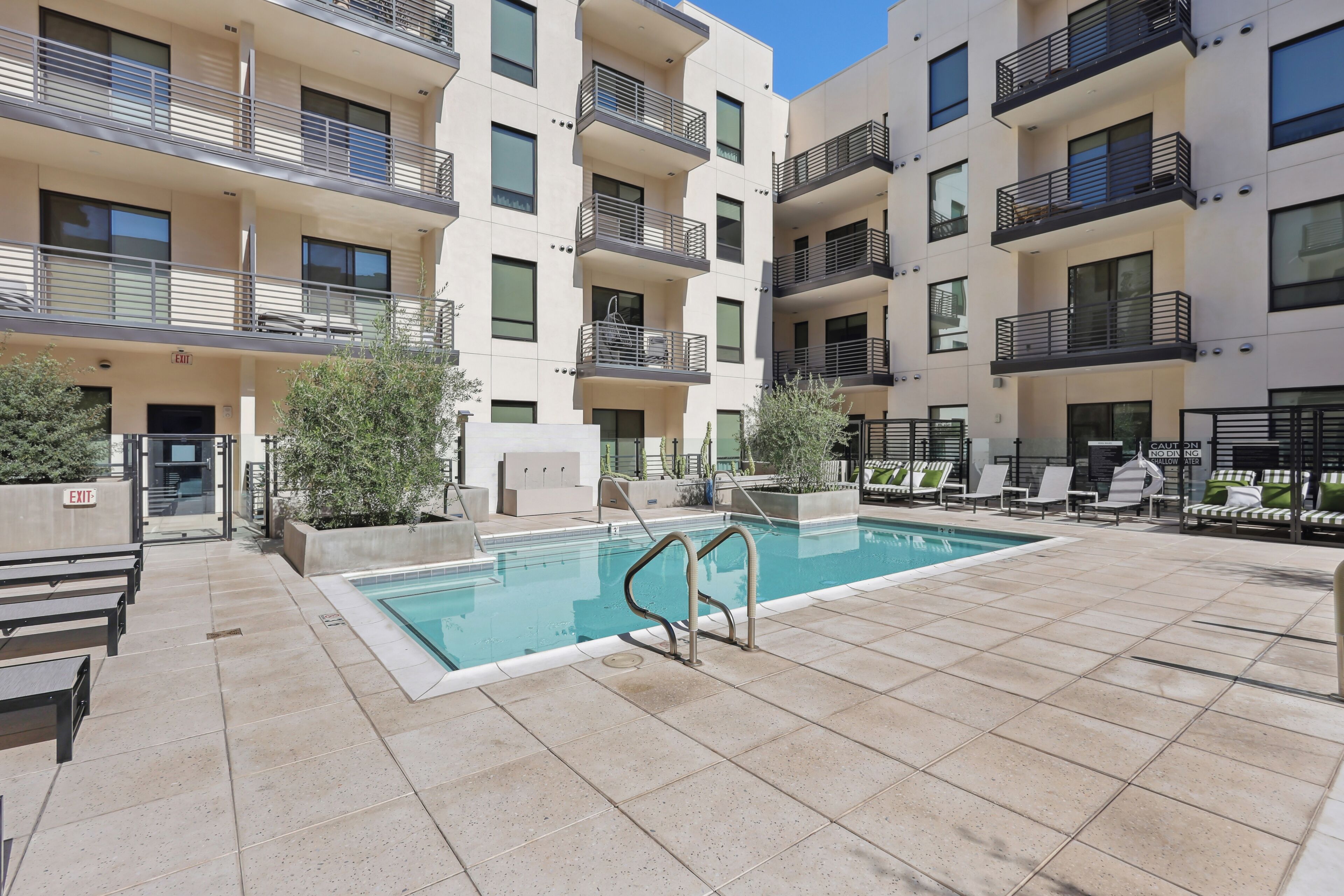 A modern apartment building with a swimming pool, outdoor seating, and a clear sky.