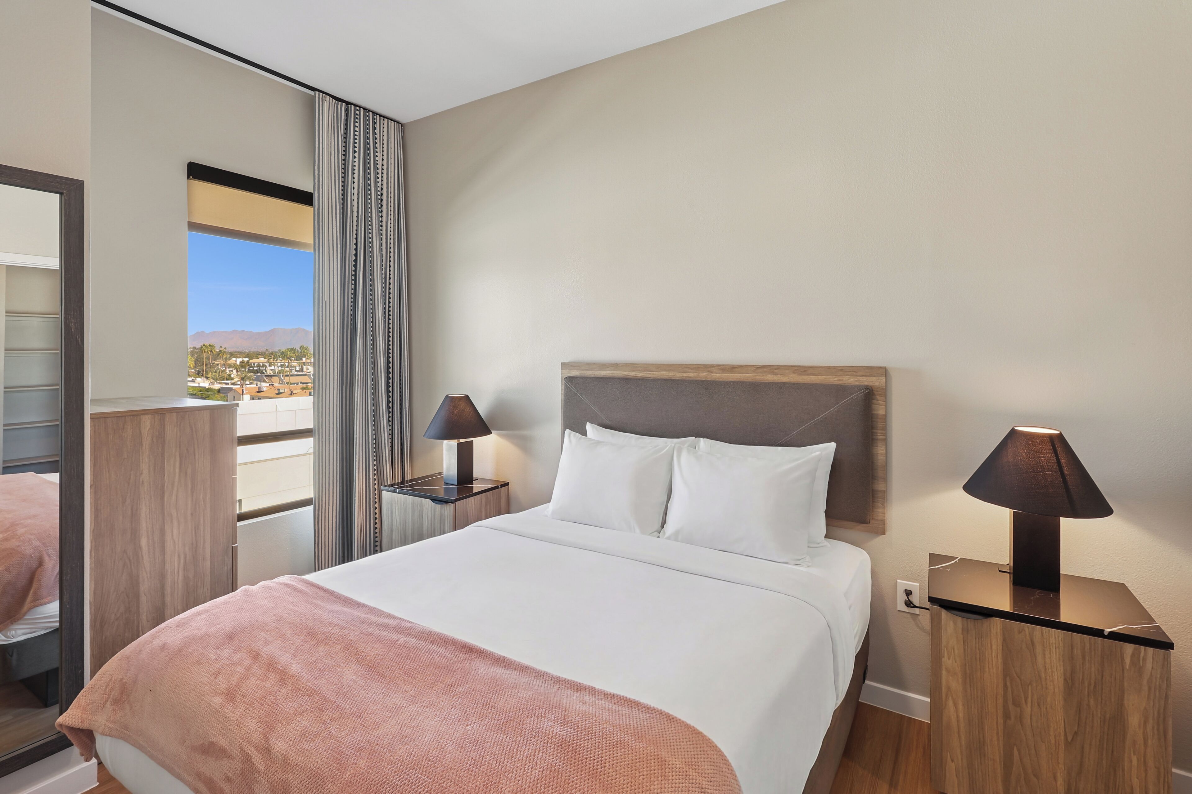 Une chambre d’hôtel avec un grand lit, deux tables de chevet avec des lampes, une fenêtre avec des rideaux et une vue sur le paysage urbain.