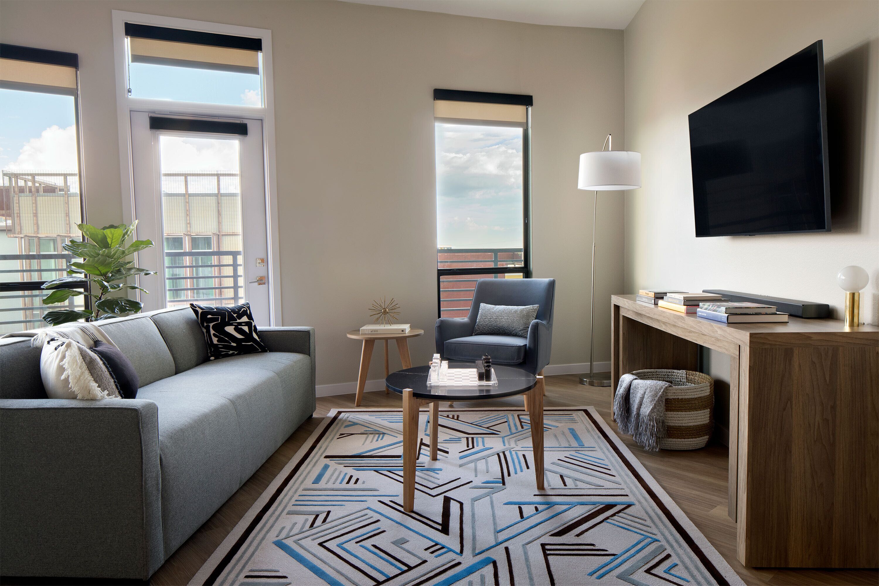 Un salon moderne avec un canapé gris, un fauteuil bleu, une table basse et un téléviseur fixé au mur.