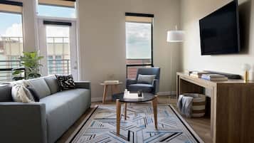 Un salon moderne avec un canapé gris, un fauteuil bleu, une table basse et un téléviseur fixé au mur.