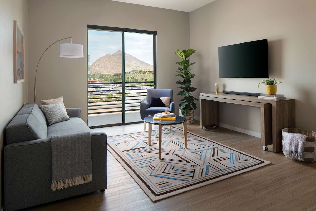 A modern living room with a sofa, a coffee table, a TV, and a large window with a mountain view.