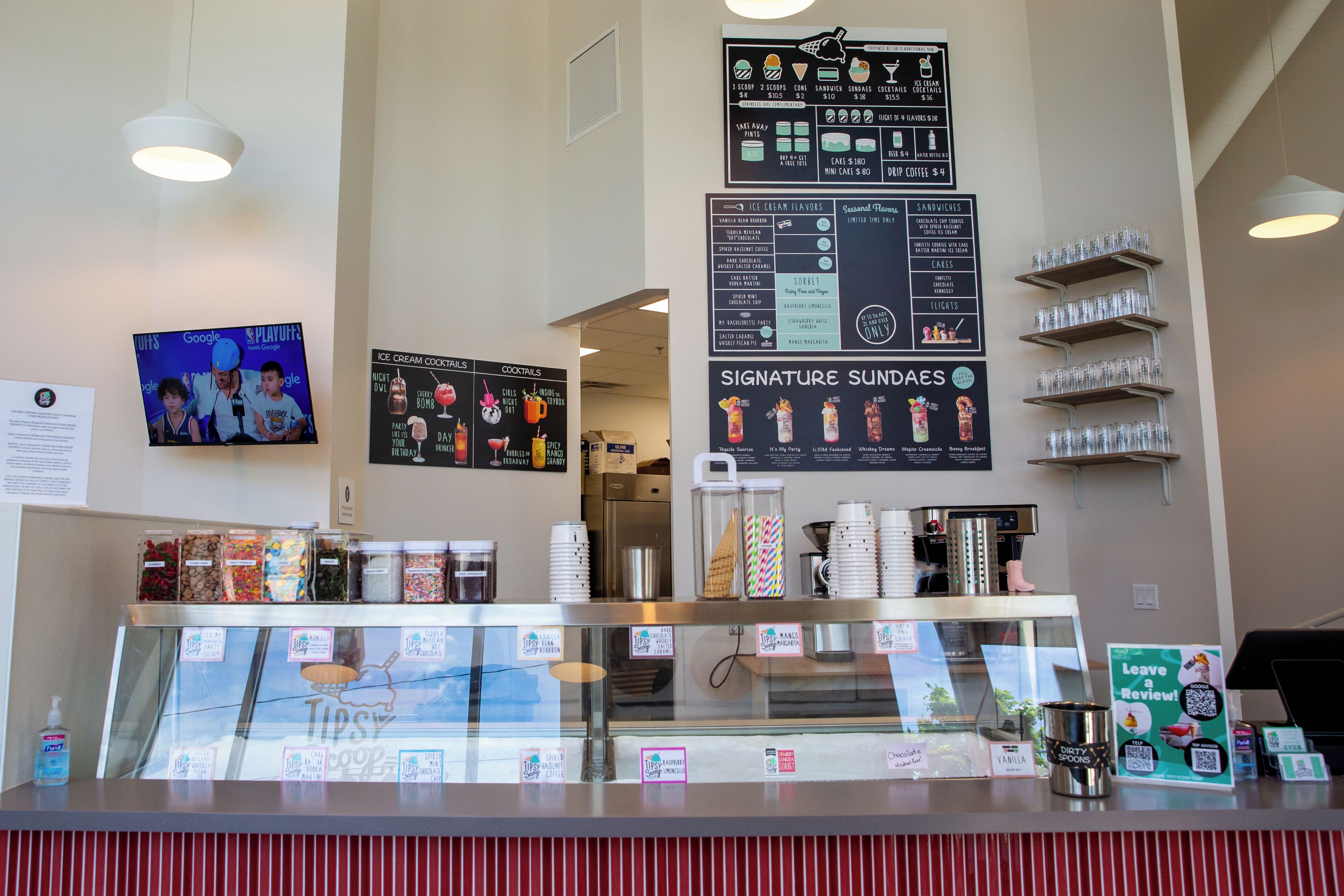 Un café avec un tableau affichant le menu, une vitrine où sont présentées les boissons et un comptoir avec un panneau.