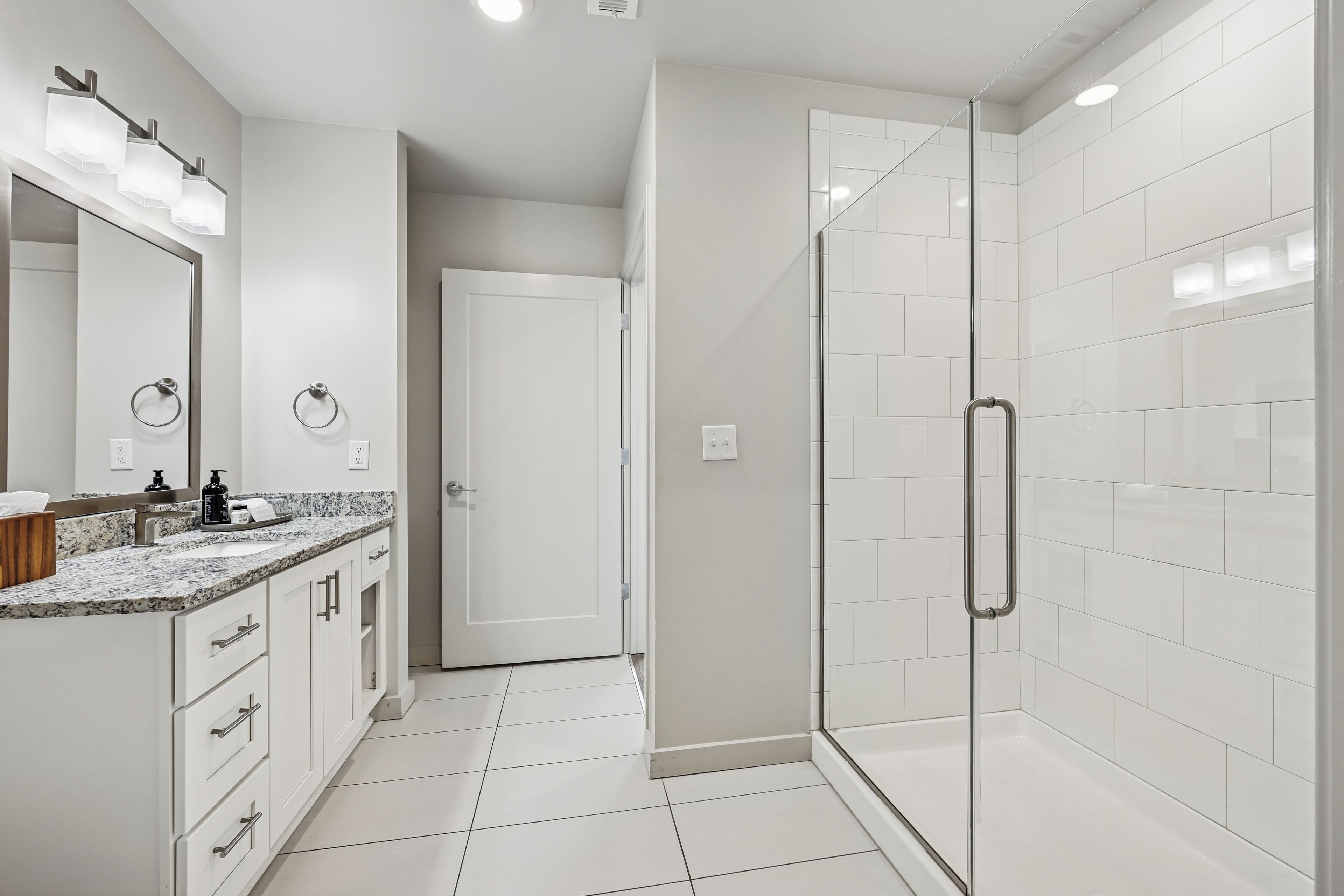 Un baño moderno con cabina de ducha de vidrio, un espejo grande y encimera de granito.