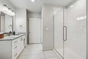 Une salle de bain moderne dotée d’une douche à parois de verre, d’un grand miroir et d’un comptoir en granit.
