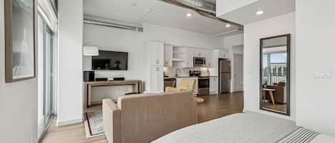 A modern apartment with a large bed, a sofa, a kitchen, and a dining area.