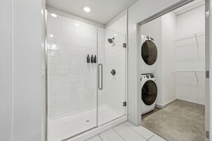 A modern bathroom with a glass-enclosed shower, a built-in washing machine, and a towel rack.