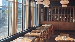 Ein Restaurant mit Holztischen und -stühlen, großen Fenstern und hängenden Papierlampen.