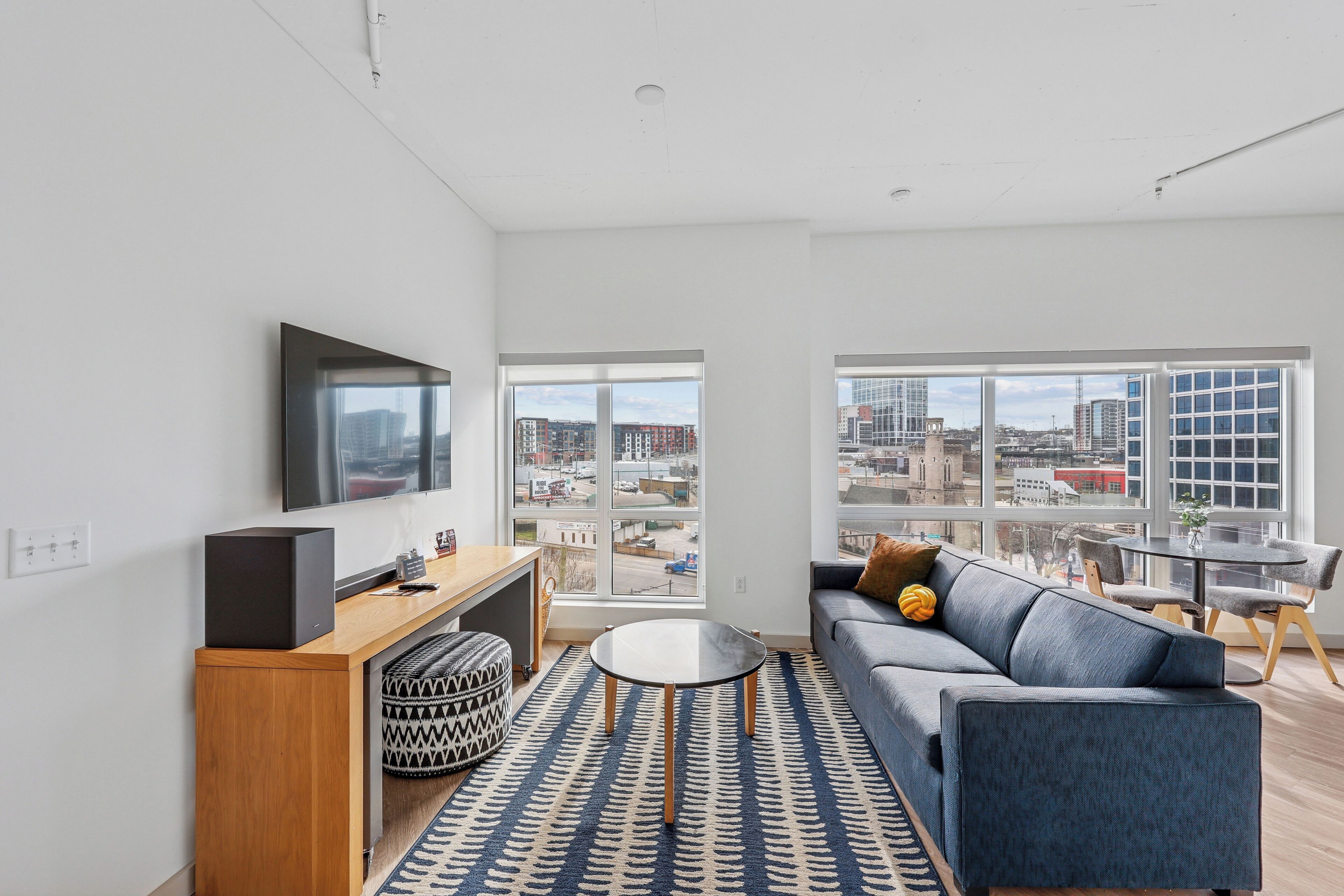 A modern living room with a sofa, a coffee table, a TV, and a city view through large windows.