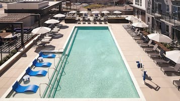 Una piscina en la azotea con tumbonas y sombrillas, rodeada de edificios.
