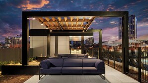 Ein Sitzbereich im Freien mit modernem Design, bestehend aus einer Couch und einem Tisch, vor einer Stadtkulisse.