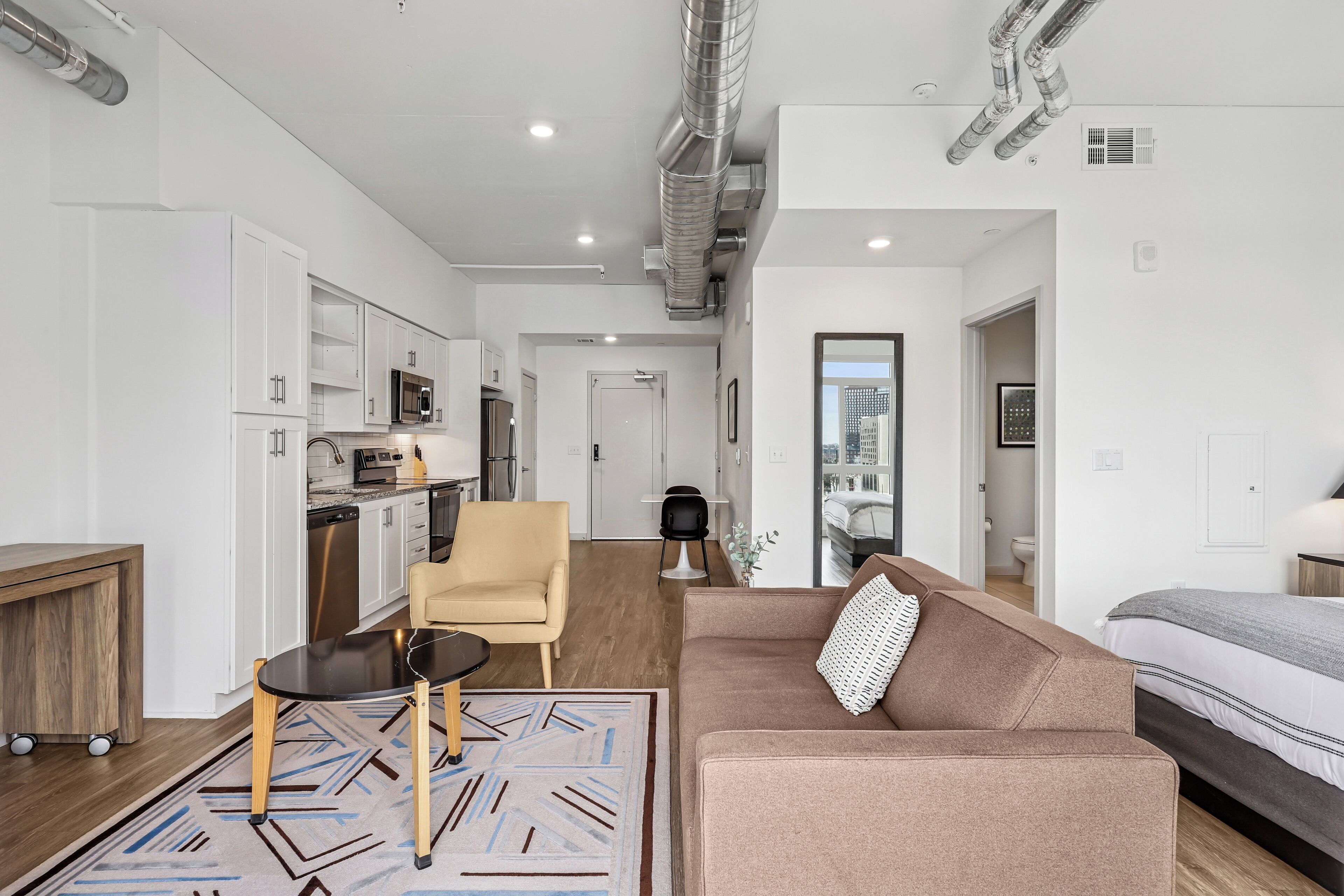 A modern apartment with a kitchenette, a living area with a sofa and a coffee table, and a bedroom with a bed.