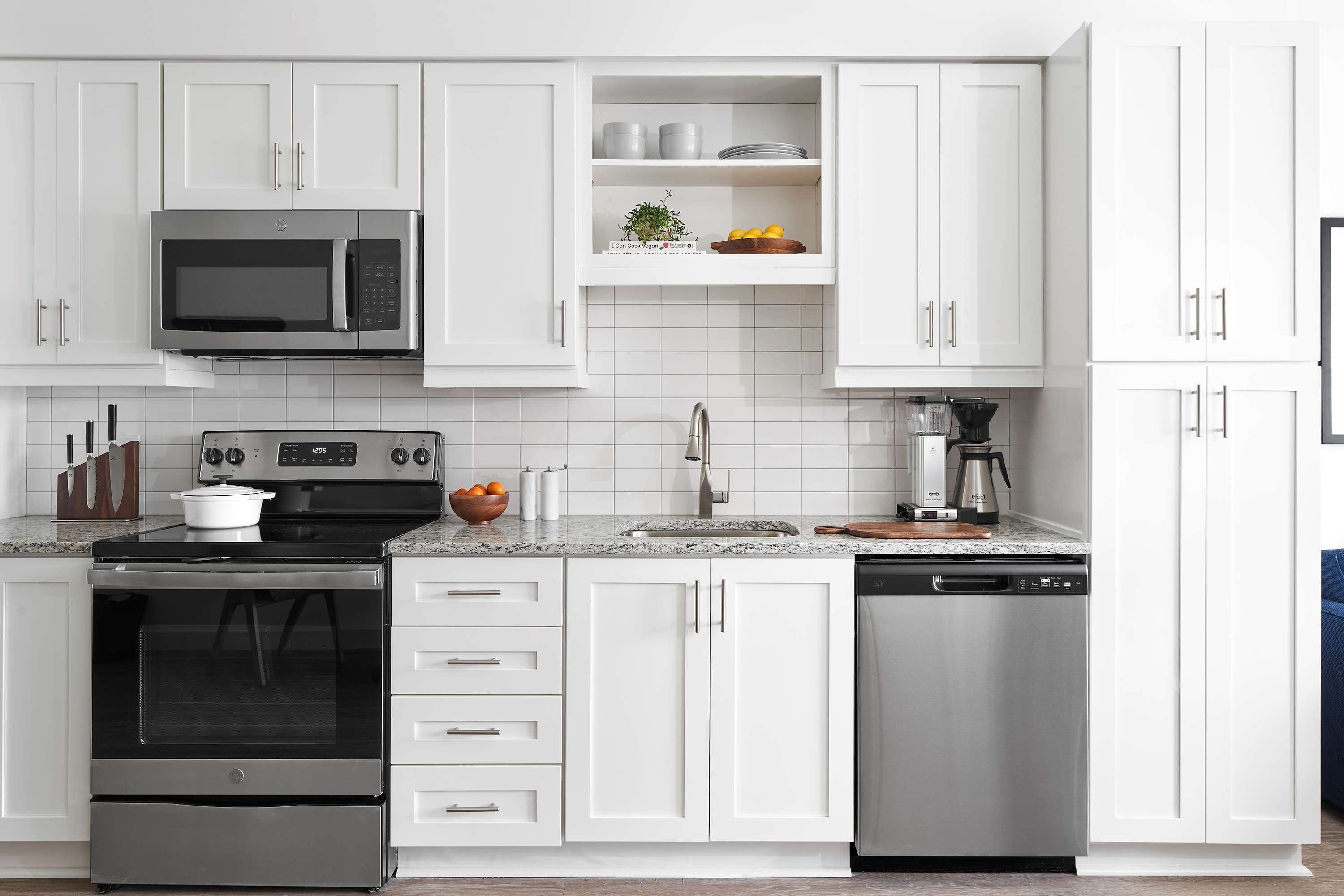 A modern kitchen with white cabinets, a stainless steel microwave, oven, and dishwasher.