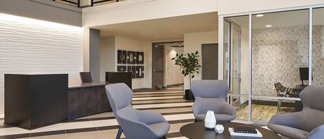Un lobby moderno con una recepción, un área de descanso y una escalera que sube a un nivel superior.