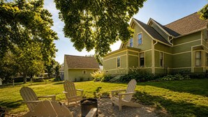 A house with a front yard, a fire pit, and four Adirondack chairs.