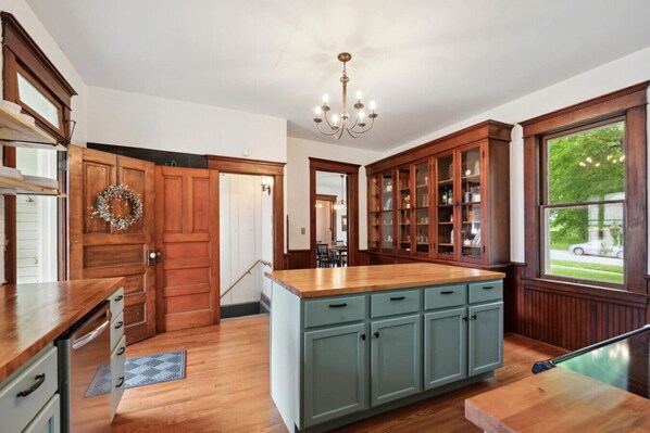 A spacious kitchen with wooden cabinets, a central island, and a chandelier. - Cloverleaf Victorian | Historic Victorian | Walk Downtown | Sleeps 10 (Pella)