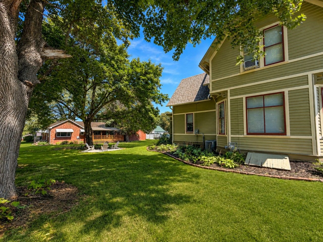 A residential property with a well-maintained lawn, a large tree, and a two-story house with a visible front porch and windows.