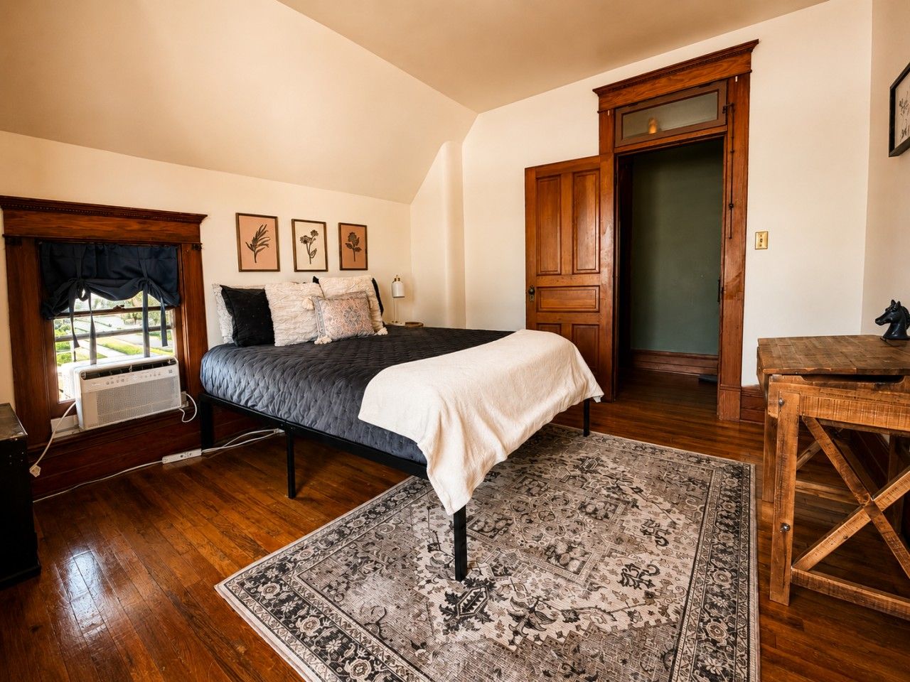 Een slaapkamer met een bed, een vloerkleed, een houten deur en een raam met gordijnen.