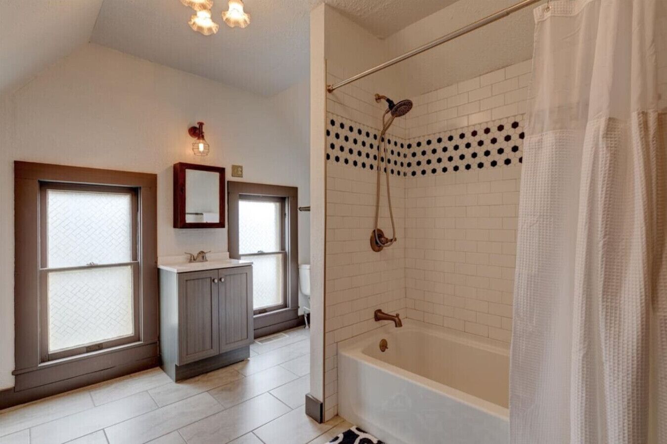 Une salle de bain avec une baignoire, une douche et deux fenêtres.