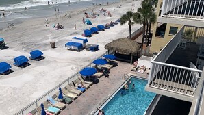 Zona de piscina con sillas de descanso y sombrillas, piscina e playa con sombrillas y gente.