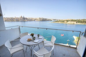 A balcony with a table set for two, overlooking a body of water with a cityscape in the background. - Spacious apartment with breathtaking views GOSLM5 (Sliema)