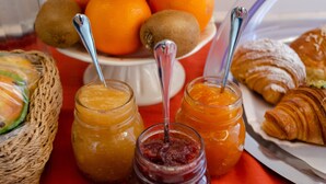 Una mesa de desayuno con una variedad de alimentos, incluyendo frutas, pasteles y frascos de mermelada.