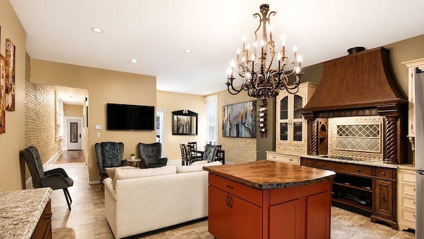 A modern kitchen with a central island, a dining area with a sofa, and a living room with a TV. - Main Street 2BR Apartment with Garage and Deck (Saint Charles)