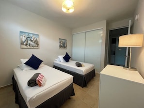 A hotel room with two beds, a wardrobe, a desk, a lamp, and two paintings on the wall.