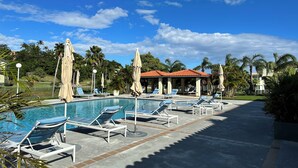 A swimming pool with lounge chairs and umbrellas, surrounded by palm trees and a clear sky. - Palmas del Mar Family Vacation Resort Spot!   (Palmas del Mar)