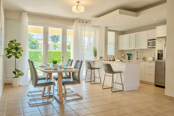 A modern kitchen with white cabinets, a central island, and a dining area with a table and chairs. - Palmas del Mar Family Vacation Resort Spot!   (Palmas del Mar)